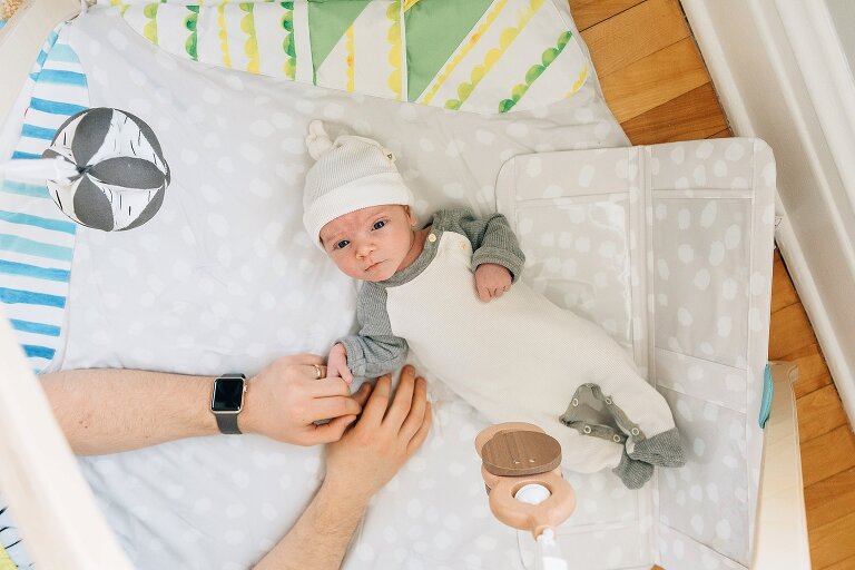 newborn looks up from playmat while Dad holds his hand