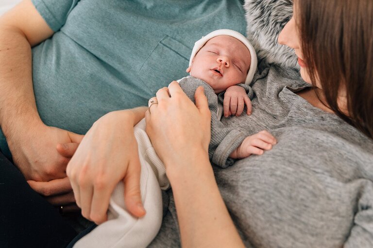 Mom holds sleeping baby while Dad lies next to her. 