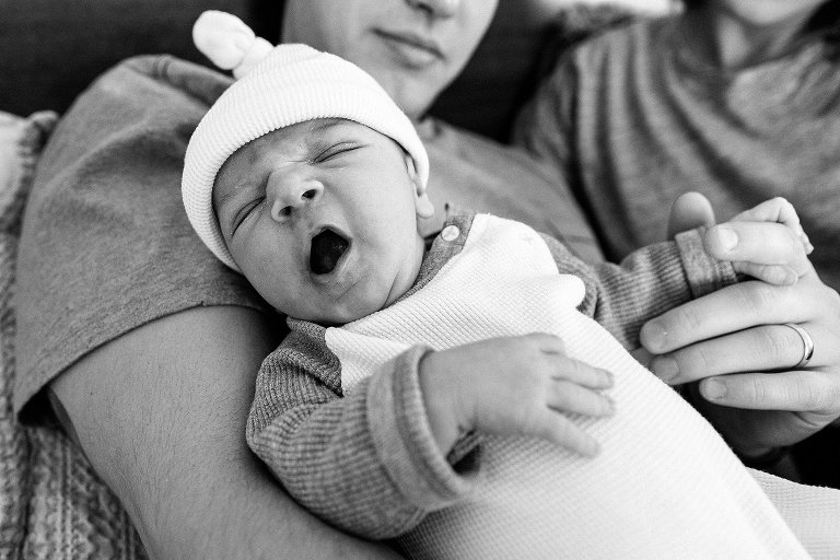 Sleepy baby yarns while dad holds his fingers 