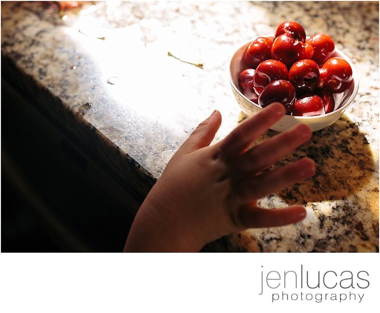 A small child hand reaches onto the counter toward a bowl of cherries 