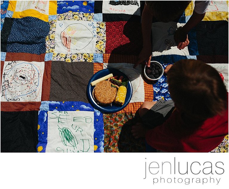 Two children have a picnic lunch on a colorful quilt 