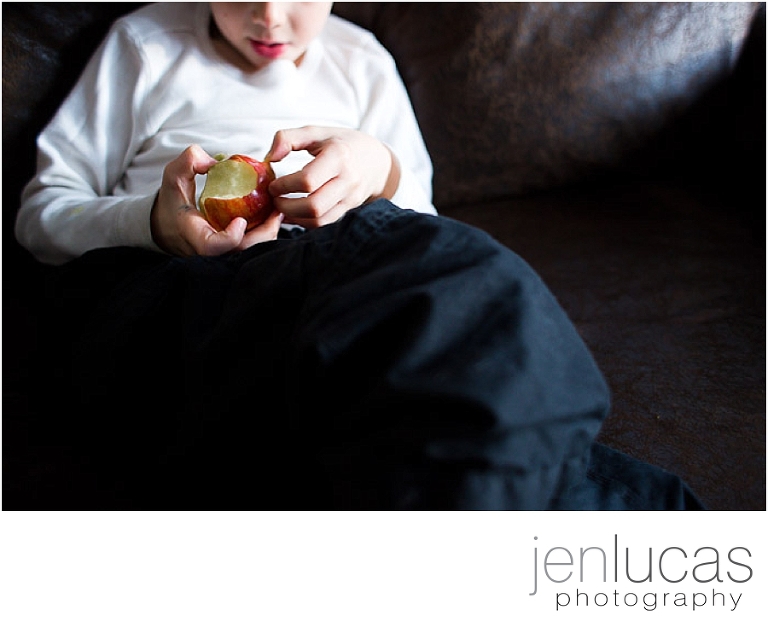 Young boy eats an apple on the couch. It has several bites out of it. 