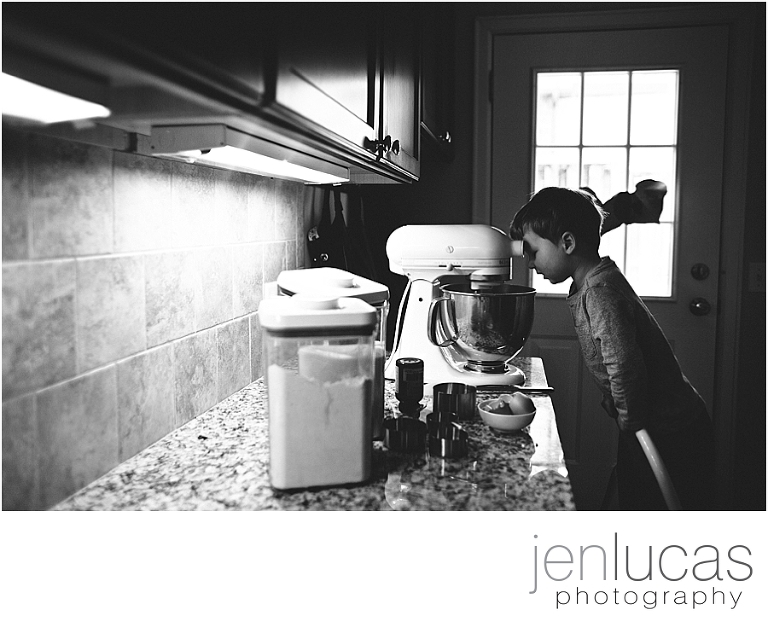 A toddler looks into the mixing bowl. Black and white. 
