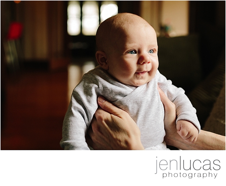 Young infant makes eye contact and smiles wiht his mother holding him. 