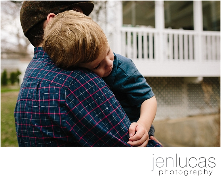 Dad holds preschool son outside in the yard. 