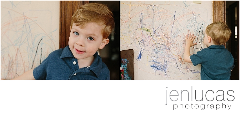 Boy stands near wall that he colored on in family home. 