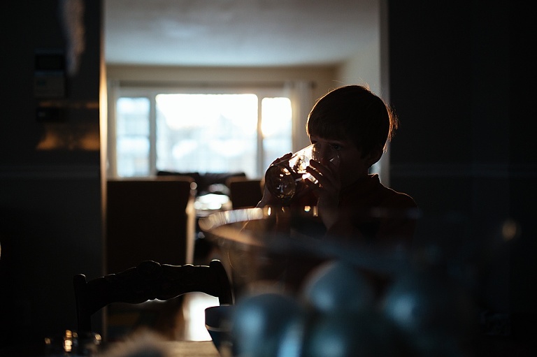 Boy drinks from glass in dark room with rim light softly illuminating his outline. 