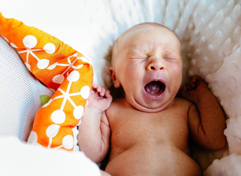 Sleeping newborn baby yawns while laying on a soft white blanket.