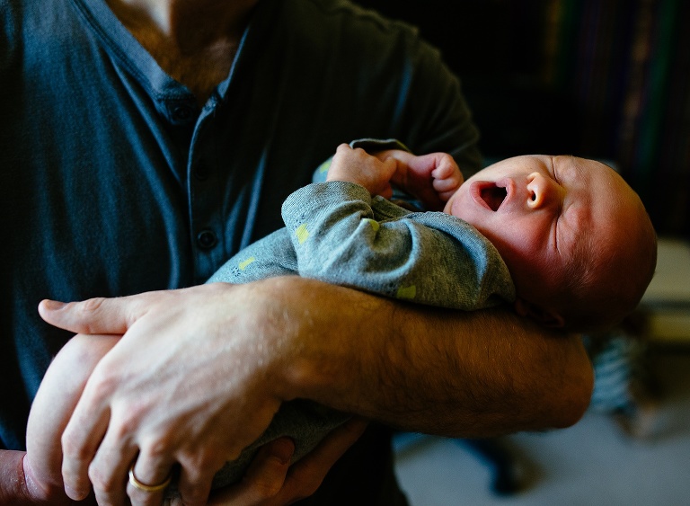 Sleeping newborn baby yawns while father holds him.