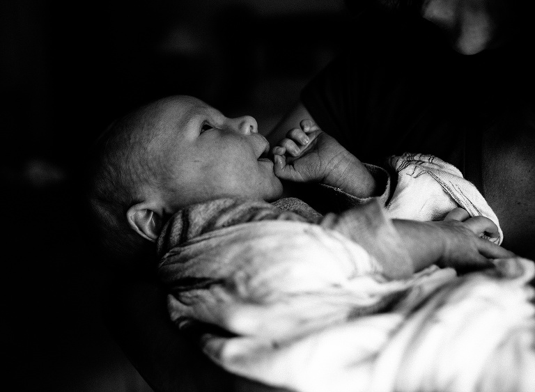Black and white. Newborn baby looks up while being held.