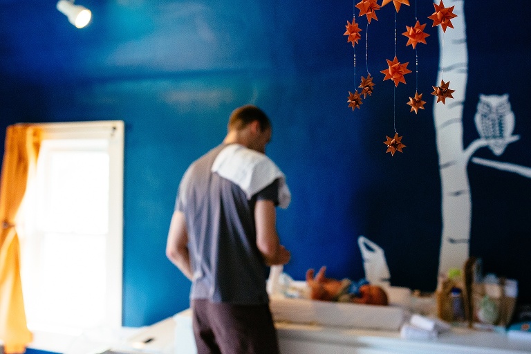 Father changes newborn baby's diaper in the baby's blue nursery.