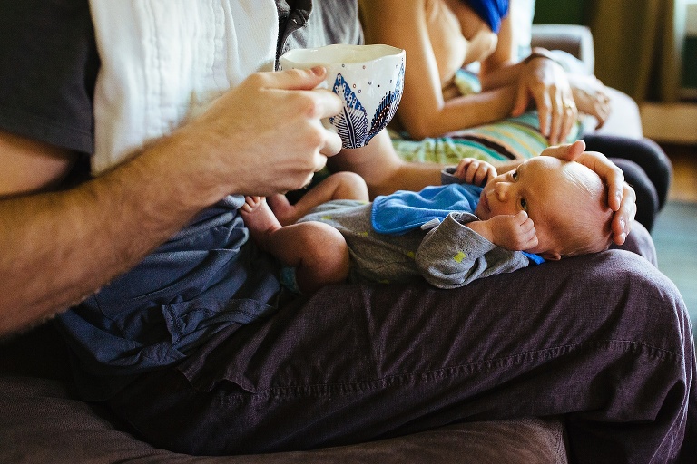 Father has newborn baby laying down on his legs as he sits a cup of coffee.