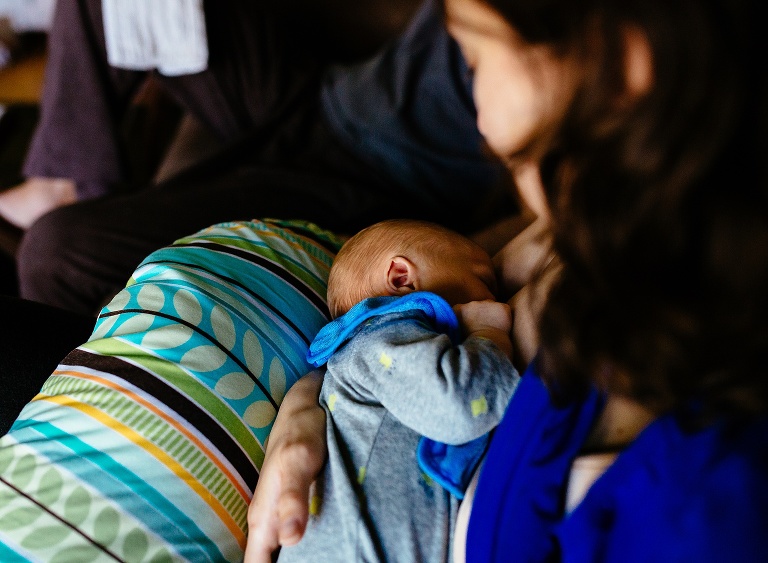 Mom sitting down on the couch breastfeeding newborn baby boy.