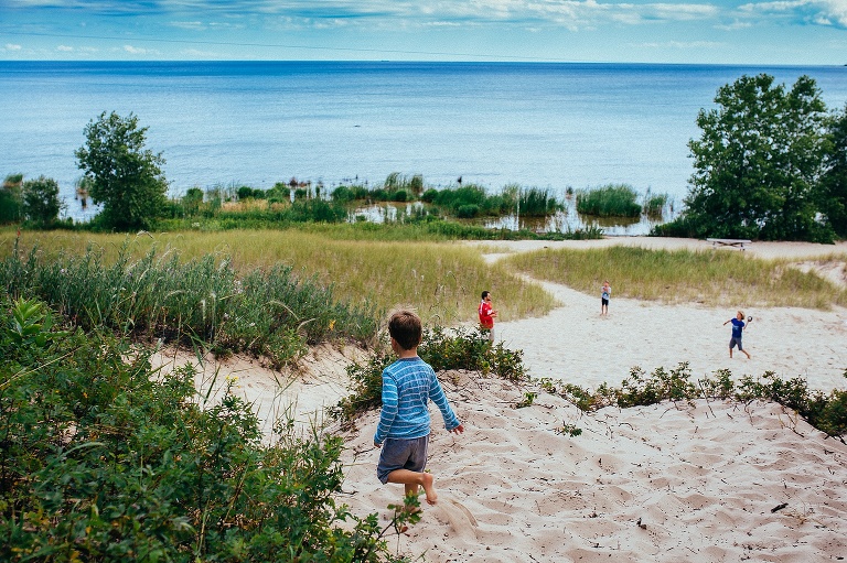 Family playing football in the sandy beach next to a big blue lake.