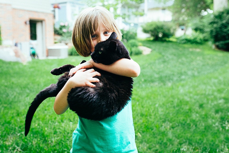 Young girl standing outside holds black cat in her arms.