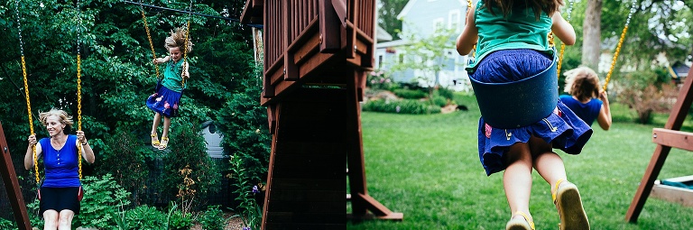 Two young kids swinging with their mom outside on the swing set.
