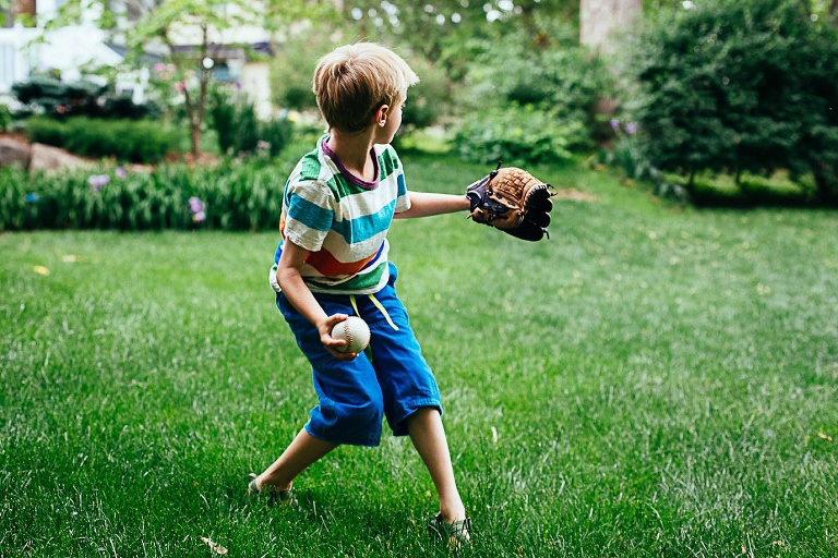 Young boy standing outside in the grass gets ready to throw a baseball.