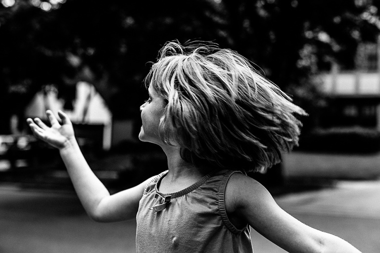 Black and white image. Young girl running outside, her hair flowing behind her.