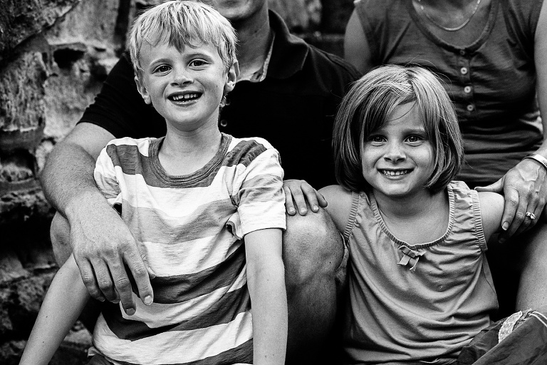 Black and white. Brother and sister sitting with their parents smile for the camera.