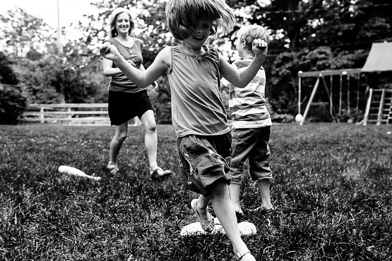 Black and white image. Young brother and sister play outside with their mom in the backyard.