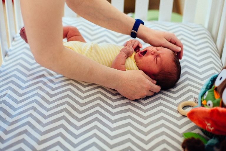 Moms arms reaching into crib to calm her crying newborn baby.