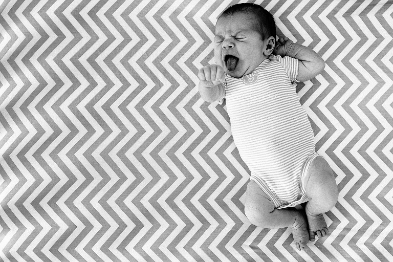 Black and white. Sleepy newborn baby laying on a chevron mattress yawns and stretches after a nap.