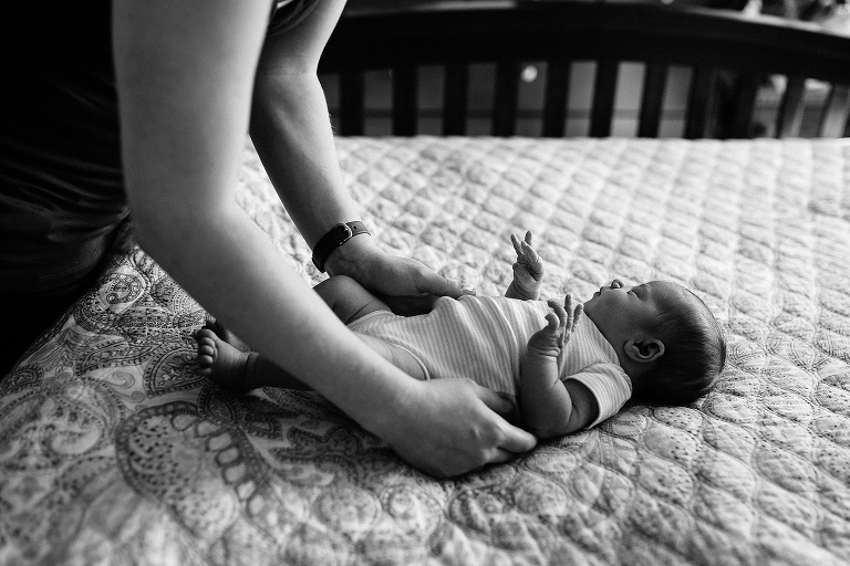 Black and white. Mom sets down her sleeping newborn baby on her bed.