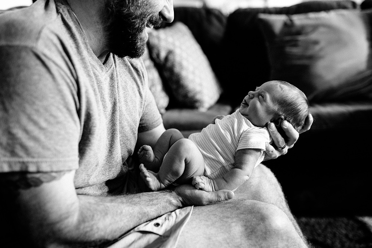 Black and white. Father smiles while holding and looking at newborn baby girl.