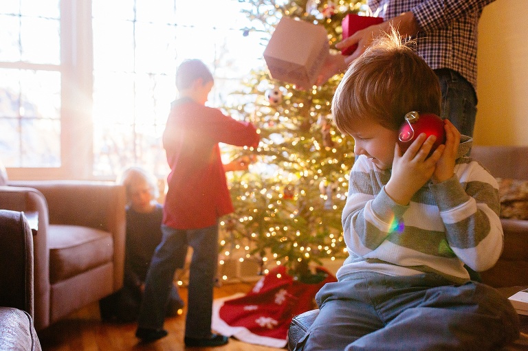 Family decorates christmas tree together. young boy holds red christmas ornament up to his ear.