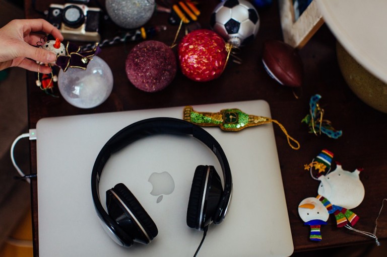Laptop and headphones sit on wood table, many christmas ornaments sit all around it.