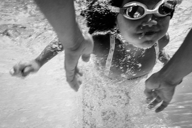 Black and white. Underwater image of young girl swimming in the pool to her mothers arms.