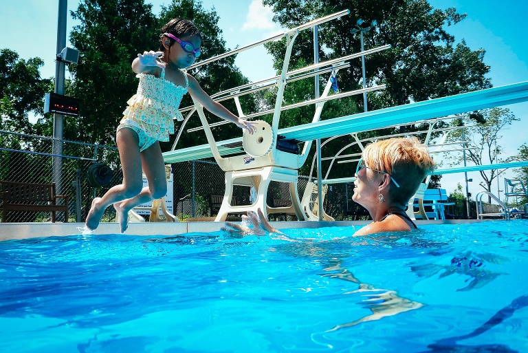 Mom stands in the water while her daughter jumps into the pool.