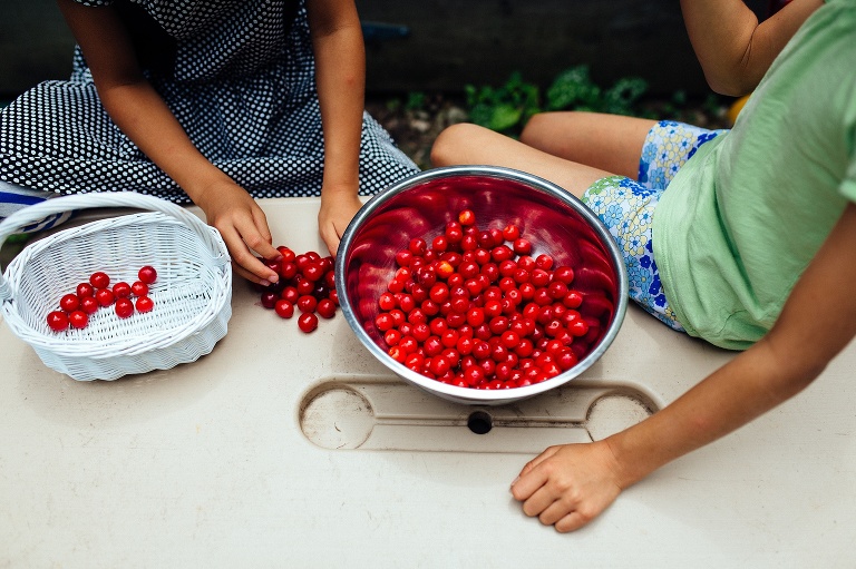 Two girls sit next to a bowl full of fresh red cherries.