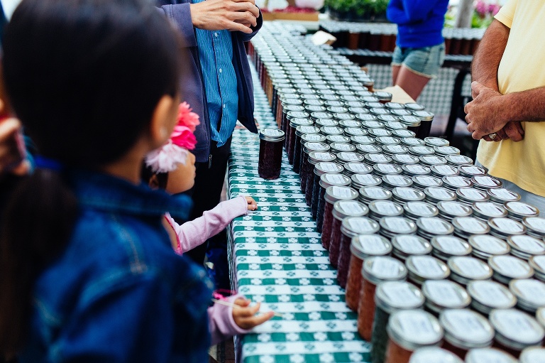 Family at a farmers market standing in front of a vendor selling jars of jam.
