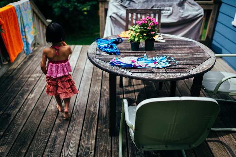 Young girl walks across back patio next to the beach towels and swimsuits set outside to dry.