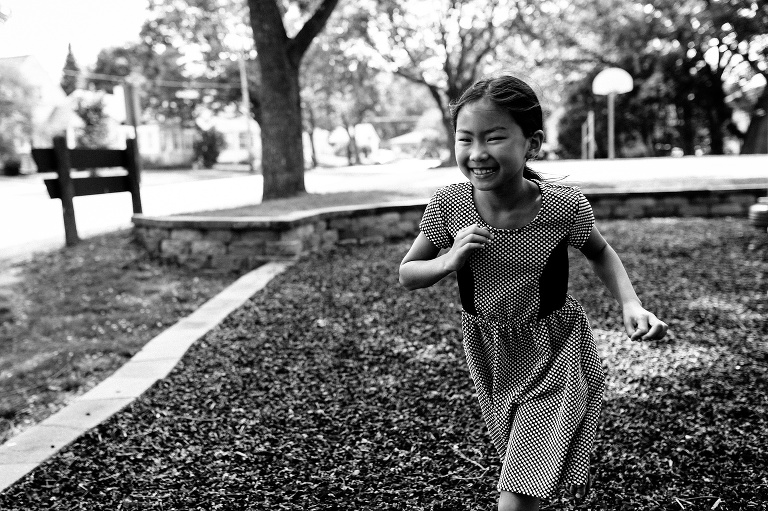 Black and white. Young girl runs across the mulch at a park playground.