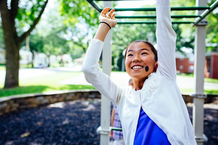 Black and white. Girl swings across monkey bars at a park playground.
