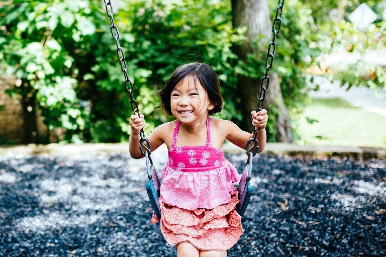 Young girl sitting on a swing with a big smile.
