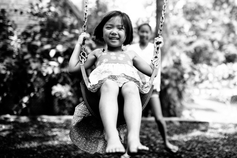 Black and white. Young girl swinging on a swing at a park.