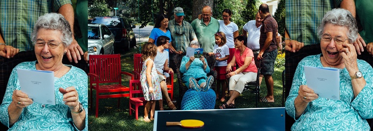 Family stands around their 90 year old mother as she reads her birthday cards.