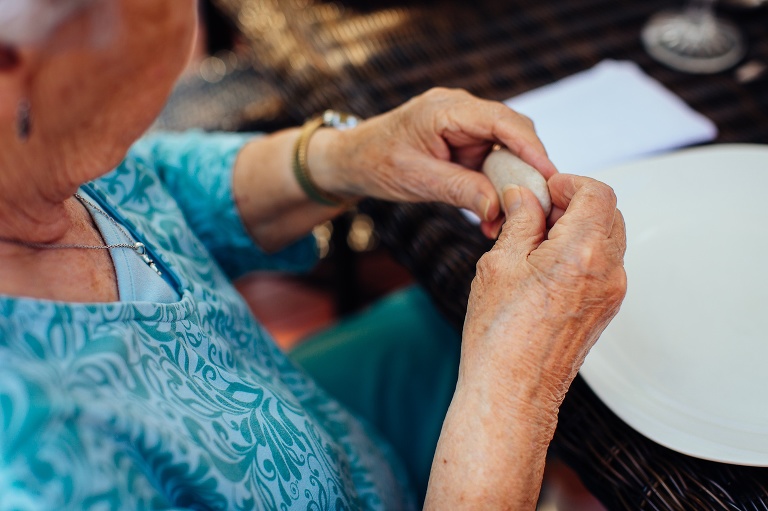 Woman holds a rock while sitting outside at dinning table eating brunch with family.