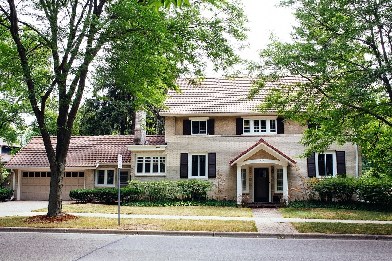 Old large brick house with black shutters. large trees all around the house.
