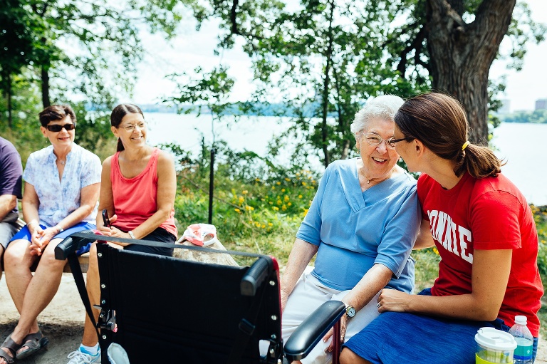 Family sitting around on a bench next to the lake celebrating mothers 90th birthday.