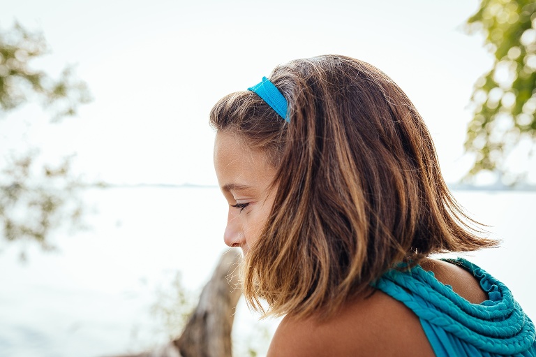 A young girl wearing blue sits outside next to a lake.