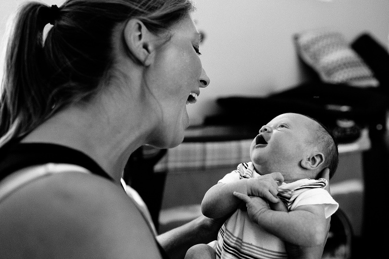 Black and white. Newborn baby looks up at his smiling mom.