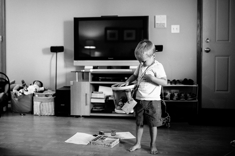 Black and white. Young boy standing in the living room holding a drum.
