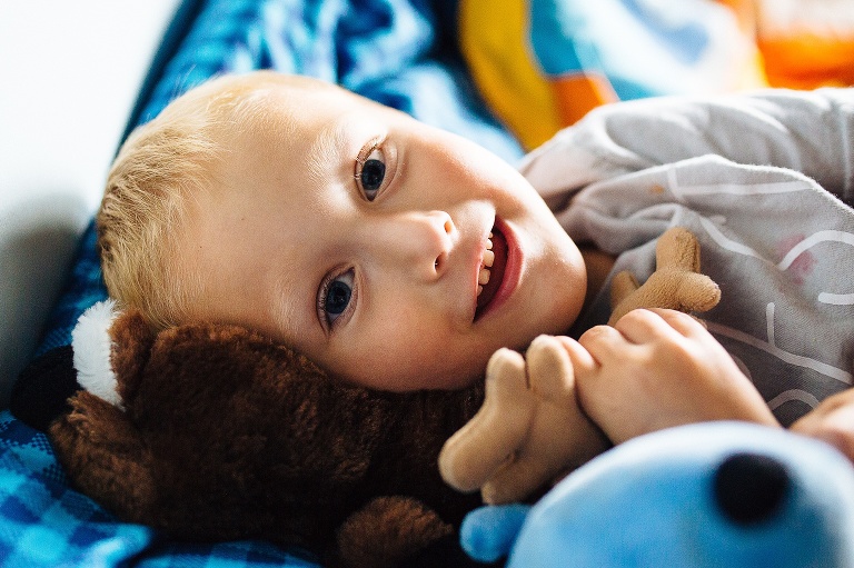 Young boy laying in bed looking up at the camera.