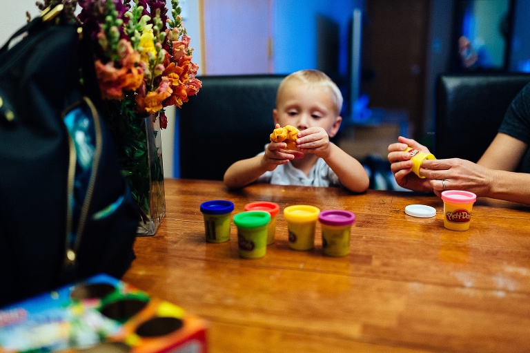 Young boy sitting at the table with his mom playing with play dough.