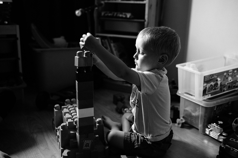 Black and white. Young boy sitting on the floor playing with building blocks.