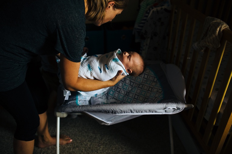 Mom sets sleeping newborn baby down in a rocking bed.